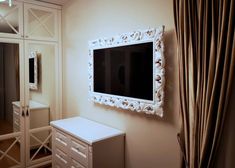 a tv mounted to the side of a wall next to a white dresser and mirror