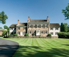 a large brick house sitting in the middle of a lush green field next to a road