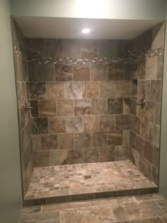 a walk in shower sitting next to a tiled wall and floor covered in brown tile