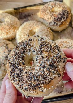 a person holding a bagel with sesame seeds on it in front of other bagels