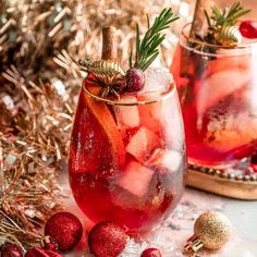 two glasses filled with red liquid and ice next to christmas decorations on the table,