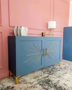 a blue cabinet sitting next to a pink wall in a room with gold accents on the doors