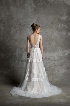 a woman in a white wedding dress standing against a gray wall with her back to the camera