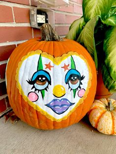 a painted pumpkin sitting on top of a wooden floor next to green leaves and a brick wall