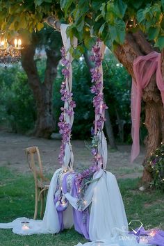 a couple of chairs sitting under a tree with flowers hanging from it's sides