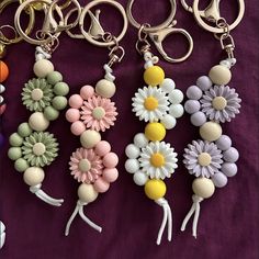 four keychains with flowers and beads on them sitting on a purple cloth background