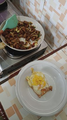 a plate with an egg on it next to a pan filled with hashbrowns