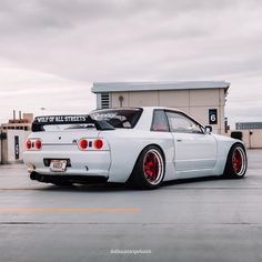 a white car with red rims parked in front of a building on a cloudy day