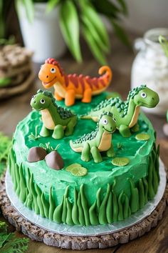 a cake with green frosting and fondant dinosaurs on top, sitting on a wooden table