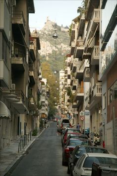 cars are parked on the side of an empty street in front of apartment buildings with mountains in the background