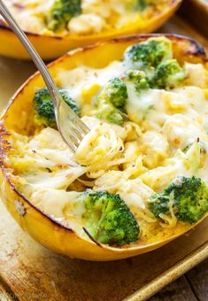 two yellow squash halves with broccoli and cheese in them on a wooden tray