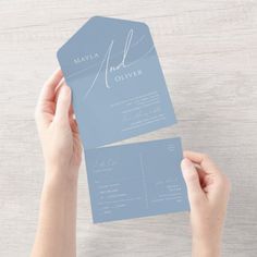 two hands holding up a business card on top of a wooden table with white and blue paper