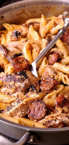 a pan filled with pasta and meat on top of a wooden table next to a fork