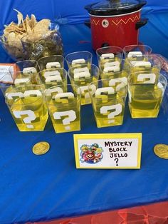 a table topped with lots of cups filled with liquid and gold coins sitting on top of a blue cloth covered table