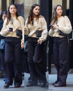 three women in black pants and sweaters are looking at their cell phones while walking down the street