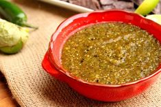 a red bowl filled with green salsa sitting on top of a wooden table next to vegetables