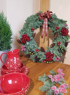 a christmas wreath sitting on top of a wooden table next to dishes and vases