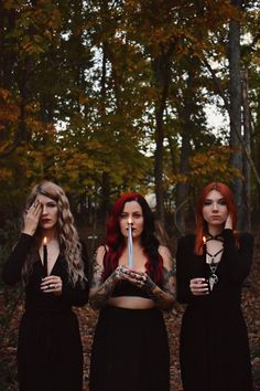 three women with red hair holding candles in their hands and wearing black clothing, standing next to each other