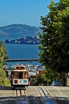 a cable car is traveling down the tracks in front of some trees and boats on the water