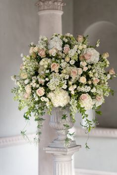 a vase filled with white and pink flowers on top of a table next to a pillar