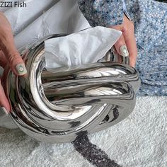 a woman is holding a silver object in her hands and it looks like they are wrapped in paper