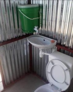 a white toilet sitting next to a sink in a room with corrugated walls and a green trash can