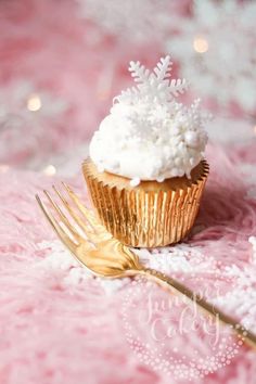 a cupcake with white frosting and a gold fork on a pink tablecloth