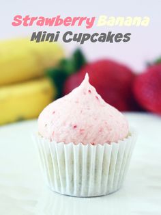 a pink frosted cupcake sitting on top of a white table next to bananas and strawberries