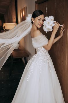 a woman in a white wedding dress holding flowers and posing for the camera with her veil over her head