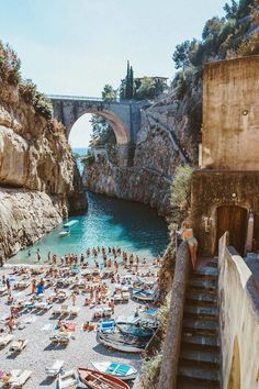 many people are laying on the beach in front of an old bridge and some boats