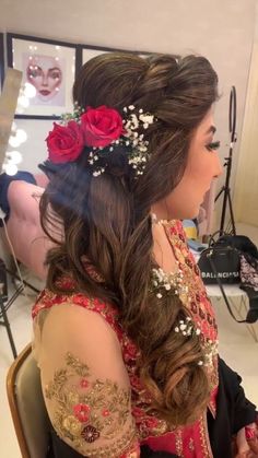 a woman sitting in a chair wearing a red and gold dress with flowers on her hair