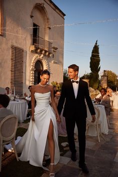 a man and woman are walking down the street holding hands while dressed in formal wear