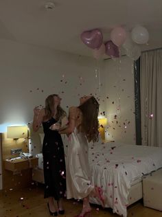 two women standing on a bed with balloons and confetti