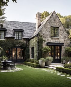 a stone house with black doors and windows is surrounded by greenery on the lawn