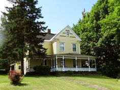 a large yellow house sitting in the middle of a lush green field next to trees