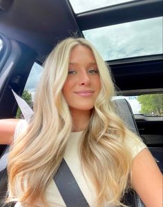 a woman sitting in the back seat of a car with long blonde hair and blue eyes