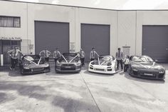 four race cars are parked in front of two garage doors and one man is standing next to them