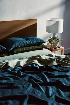 an unmade bed with blue sheets and green pillows on it, next to a lamp