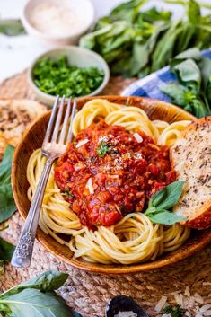 a bowl filled with spaghetti and sauce on top of a table next to bread slices