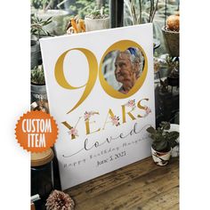 a sign with the words 90 years loved in gold on it next to potted plants