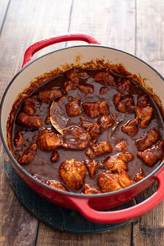 a red pot filled with meat and gravy on top of a wooden table