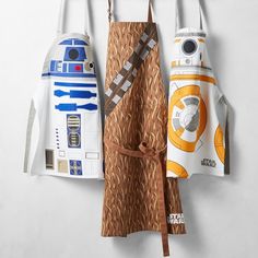 three star wars aprons hanging from hooks on a wall, one with a r2d2 and c - 3po