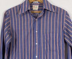 Here's a styling late 60's / early 70's vertical striped oxford button down shirt with a cool University Shop "77" original label. This well tailored shirt has a lovely lightweight permanent press cotton blend textile that's blue on blue with red and yellow offset highlighting. You'll love it's swanky vibe and look real cool in it. This 'Seven Seven' line original is in overall good condition with some pilling and a slight pullin the back that's very hard to notice. The last photo close up show Cotton Shirt With Vertical Stripes For Daywear, 1970s Style Cotton Shirt For Spring, Retro Striped Button-up Shirt, Retro Cotton Shirt With Striped Collar, Cotton Vertical Stripes Collared Shirt, Vintage Cotton Tops With Vertical Stripes, Retro Shirt With Spread Collar For Spring, Retro Button-up Shirt For Daywear, Retro Spread Collar Shirt For Spring