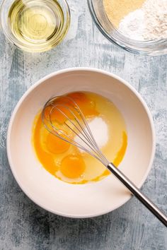 an image of eggs in a bowl with whisk and seasoning on the side