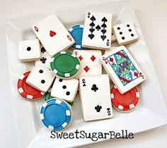 cookies decorated with playing cards and chips are on a white plate that says sweet sugar pelle