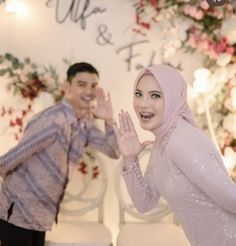 a man and woman standing next to each other in front of a wall with flowers