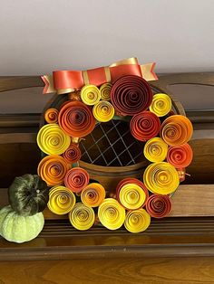 a wreath made out of rolled paper sitting on top of a wooden shelf next to a pumpkin