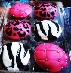 six decorated cupcakes with pink and black frosting in a plastic container on a table