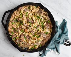 a skillet filled with pasta and meat on top of a white counter next to a blue towel