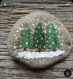 a rock painted with trees and snow on it, sitting on top of a wooden table